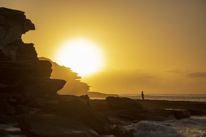 Silhouette of person standing on rock near ocean during sunset