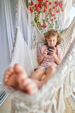 Focused boy relaxing in hammock with smartphone