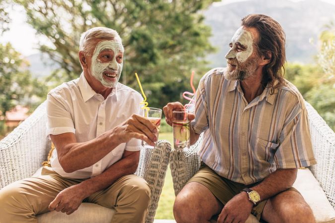 Two older friends with facial clay mask on clinking juice glasses