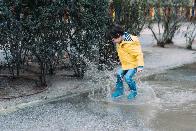 Happy kid jumping on puddle