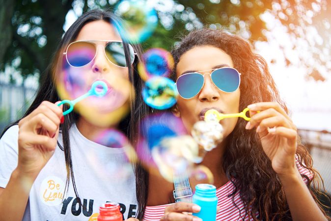 Playful young women blowing bubbles together toward camera