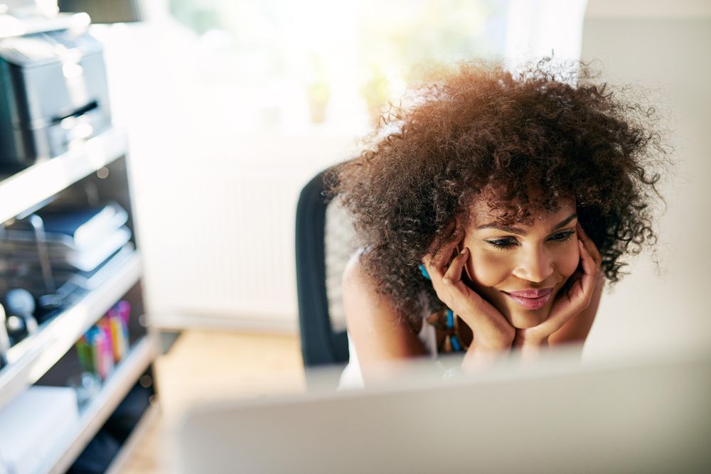 Content female with curly hair resting her chin in her hands in front of her work computer
