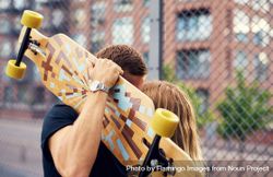 Cute couple kissing with man holding a skateboard, hiding them 5aLGa0