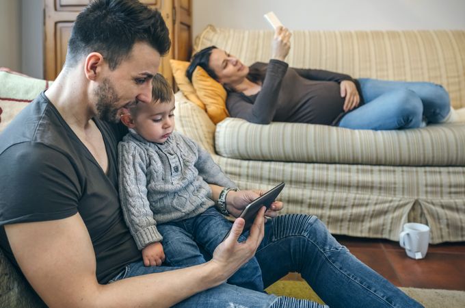 Father looking tablet with little son while the pregnant mother drinks tea