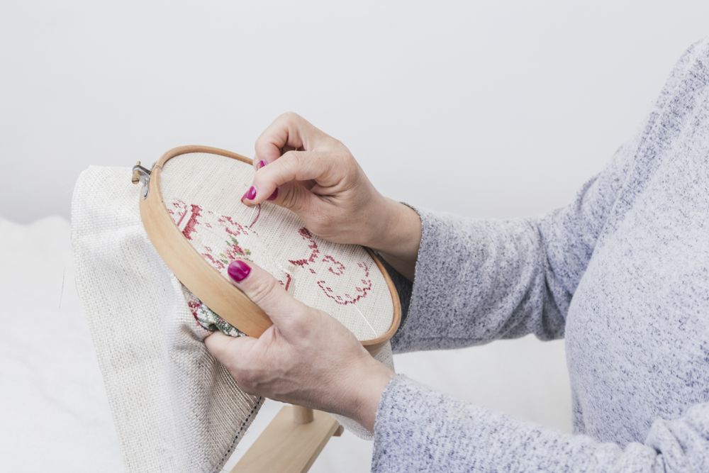 Woman's hand cross stitching pattern on a hoop against bright background