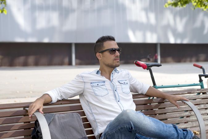 Male in denim shirt relaxing on city bench outside