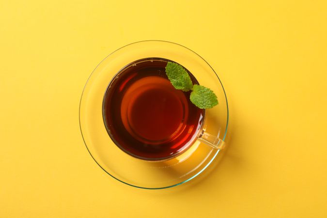 Cup of tea and mint leaves on yellow background, space for text