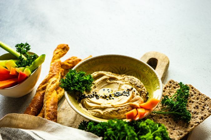 Traditional hummus dip in bowl on board served with veggies and rye crackers