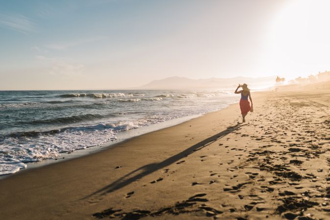 Woman holding hat and walking along seaside
