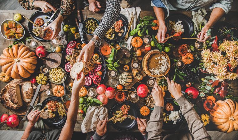 Group of people serving food at festive table with roast chicken, squash and pie