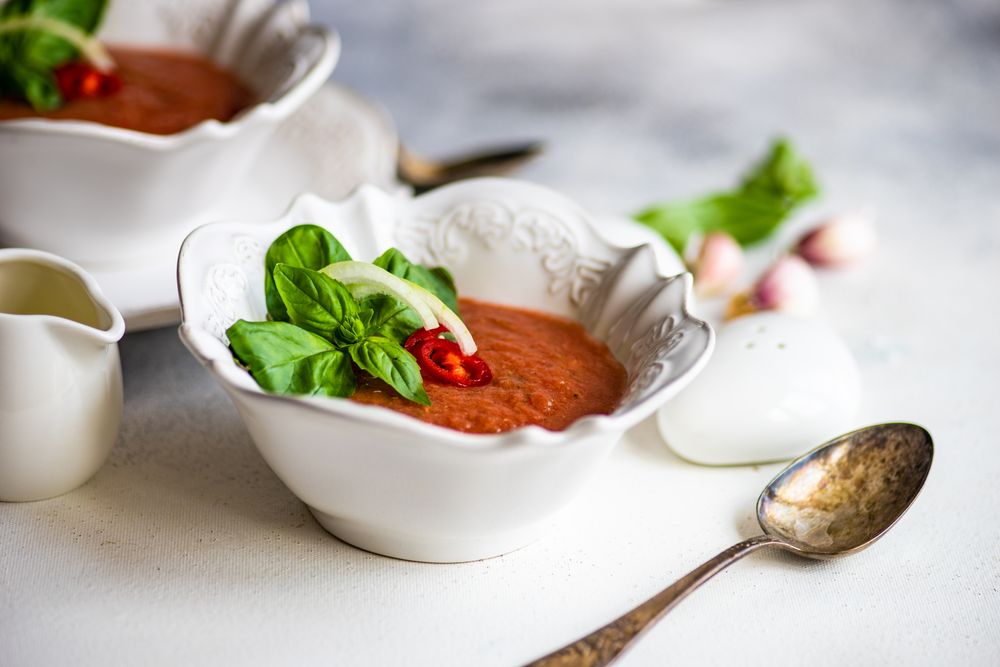 Bowls of gazpacho soup with basil, garlic, and salt and pepper shakers