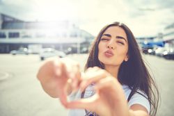 Brunette woman pushing lips making heart shape with hand
