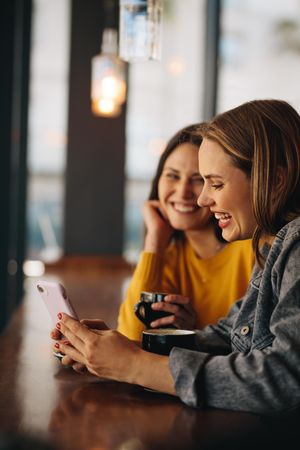 Young friends sitting in a cafe looking at a smartphone and smiling