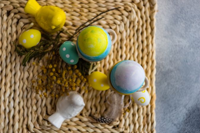 Top view of Easter table setting with with bird ornament and decorative eggs in cups on placemat