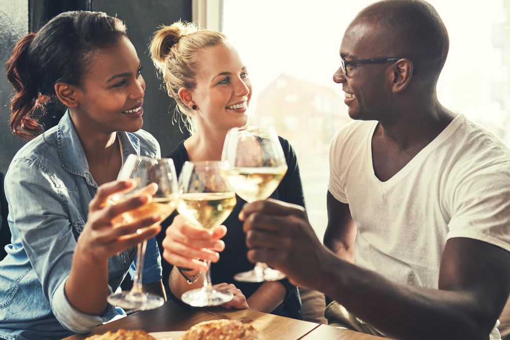Three good friends toasting with wine glasses in a bright restaurant