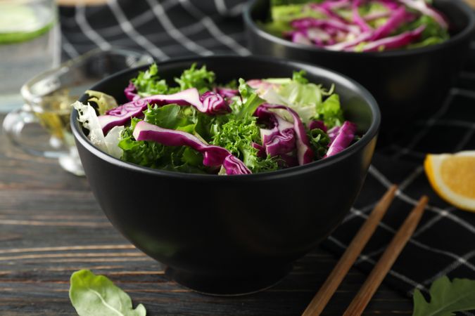Black bowls with salad, chopsticks and towel on wooden background, close up