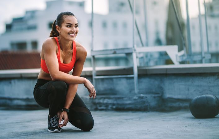 Smiling fitness woman sitting on her knee and relaxing on rooftop