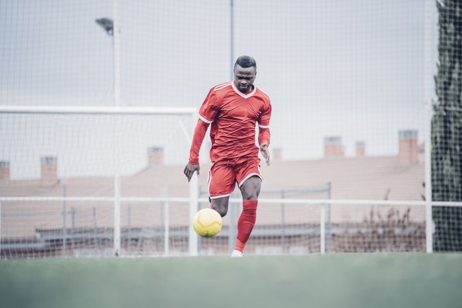 Black soccer player with red outfit playing soccer.
