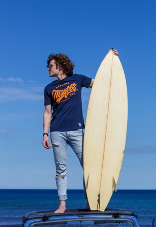 Man with surfboard standing on roof of car