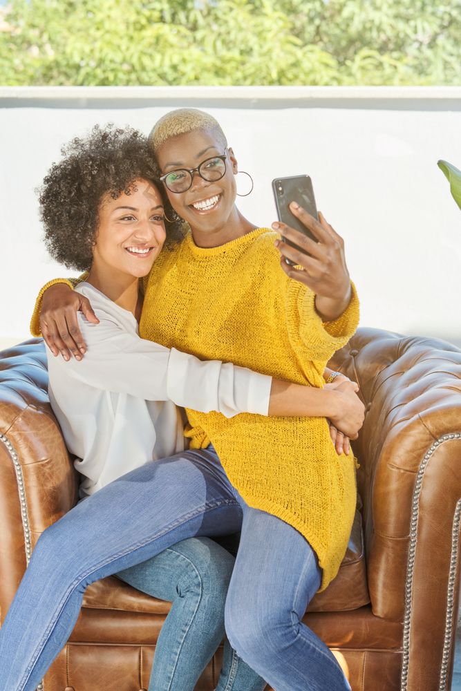 Cheerful multiracial couple of women hugging and taking self por