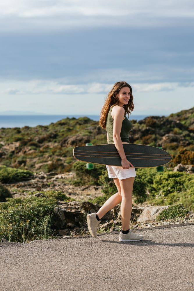 Smiling skater with longboard walking on pavement against mount
