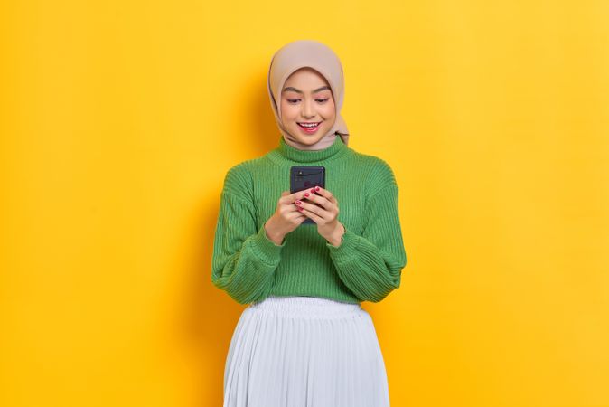 Woman in headscarf smiling and looking down at her smart phone