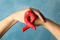 Two hands depict AIDS awareness sign against blue background, close up