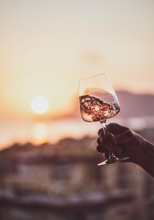 Man's hand swirling glass of rose wine against sunset, vertical composition