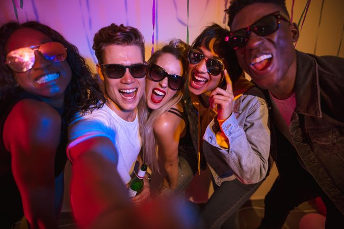 Young men and women wearing sunglasses and having fun at a colorful house party