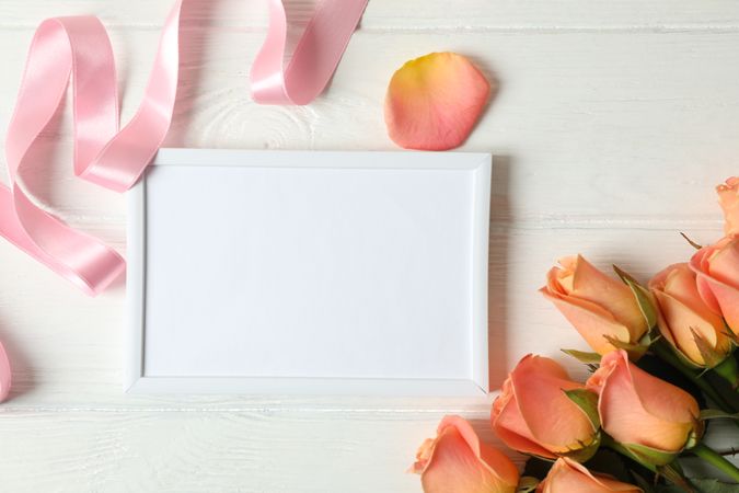 Beautiful pink roses, ribbon and empty frame on wooden background space for text