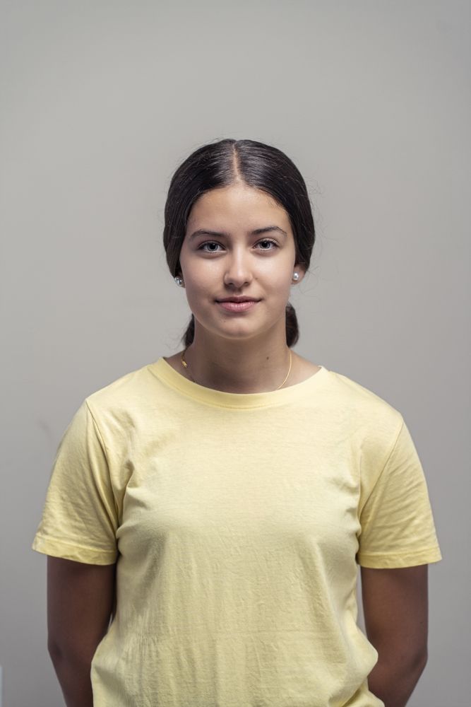 Confident teenage girl in yellow t-shirt standing still against neutral background