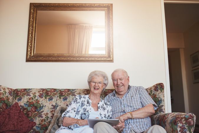 Portrait of smiling older man and woman sitting together with a digital tablet