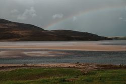 Dim rainbow over Scottish coast at sunset