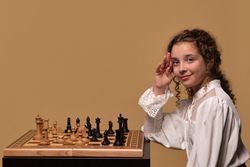 Girl smiling while raising hand in gesture near chessboard.