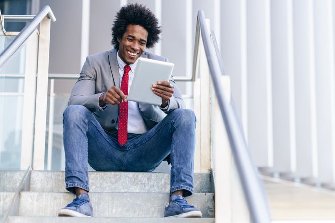 Smiling man sitting on stairs looking at his digital tablet