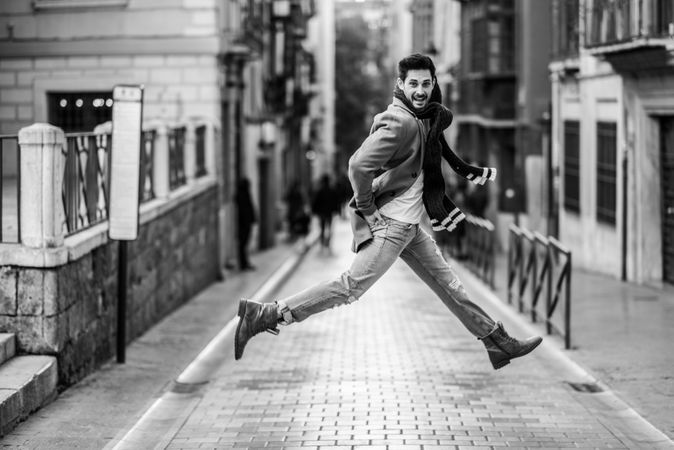 Happy man jumping while wearing winter clothes in the street