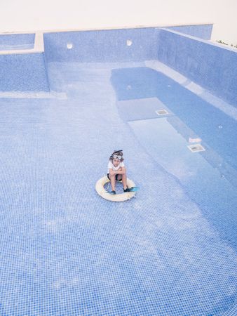 Kid with lifebuoy sitting in empty pool