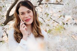 Woman answering phone call near blooming trees