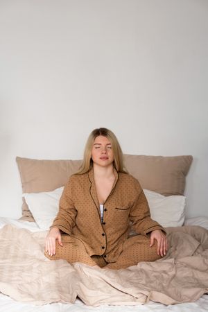 Woman meditating in pajamas on bed
