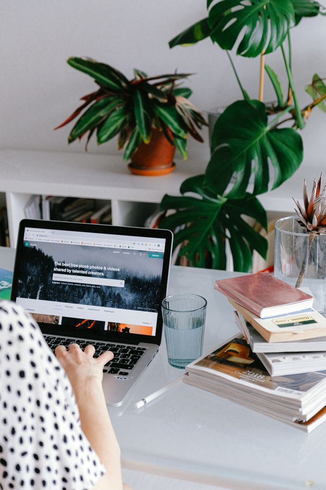 Cropped image of woman using laptop beside stack of books