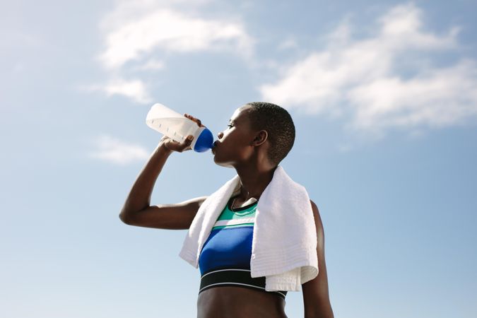 Fit woman drinking water against sky