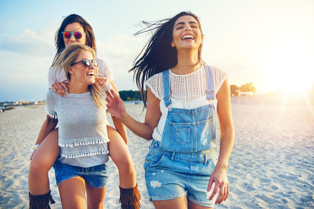 Three happy female friends having fun together walking along beach front
