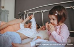 Portrait of content little girl eating cookies in bed next to her mother and brother 5qd710