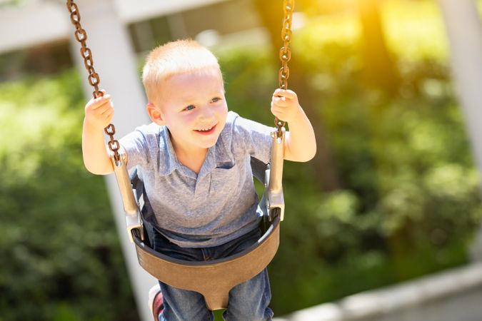 Happy Young Boy Having Fun On The Swings At The Playground