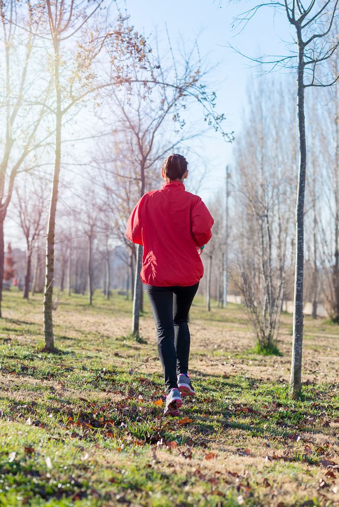 Back of active woman in red jogging outdoors in the grass on sunny fall day
