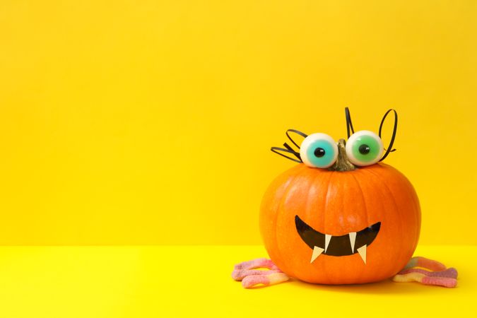 Decorated pumpkin with candy eyes on yellow background