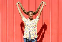 Woman holding up her braids in front of a red wall