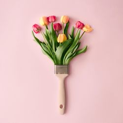 Paint brush and colorful tulip flowers on pastel pink background