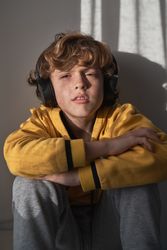Pensive child listening to songs in headphones at home