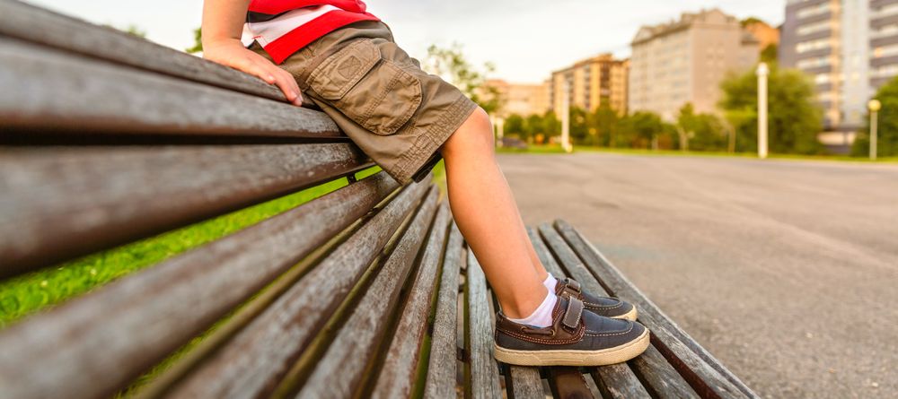 Boy legs sitting on the top of bench park relaxing